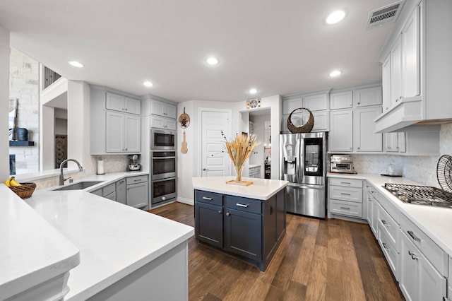 kitchen featuring visible vents, a kitchen island, appliances with stainless steel finishes, light countertops, and a sink