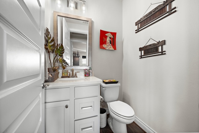 half bathroom with wood finished floors, vanity, toilet, and baseboards