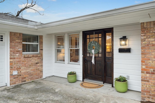 doorway to property with a garage, a shingled roof, and brick siding