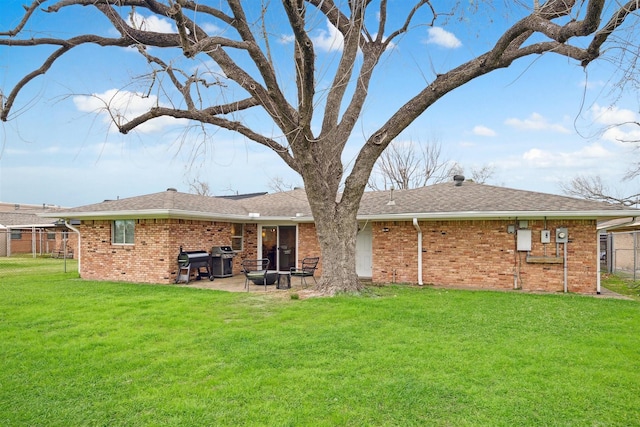 rear view of house with brick siding, a lawn, a patio area, and a shingled roof