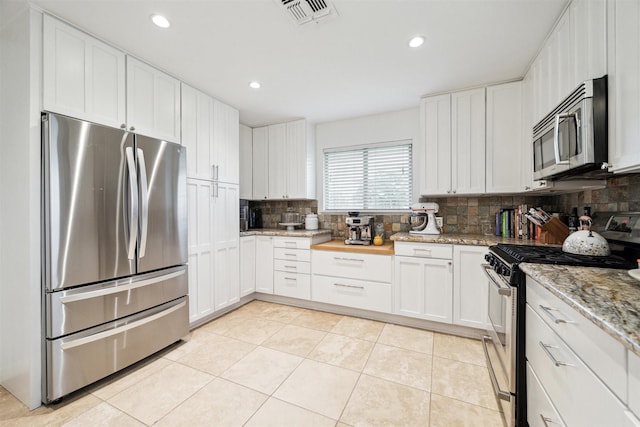 kitchen with appliances with stainless steel finishes, white cabinets, visible vents, and light stone counters