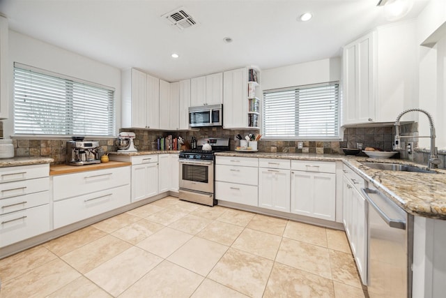 kitchen with visible vents, white cabinets, light stone countertops, stainless steel appliances, and a sink