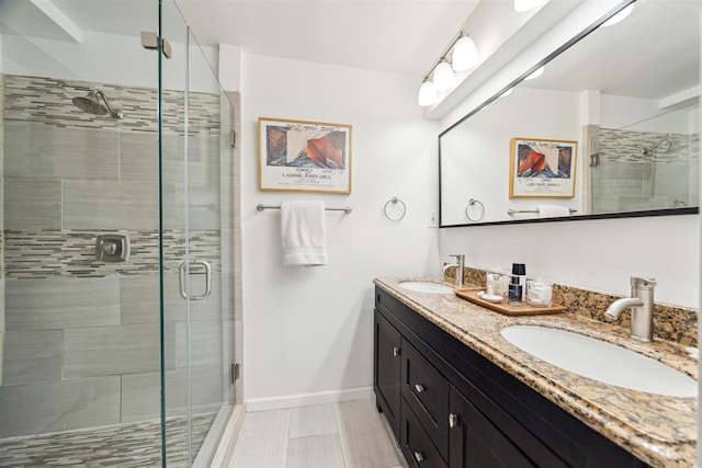 bathroom featuring a sink, a shower stall, baseboards, and double vanity