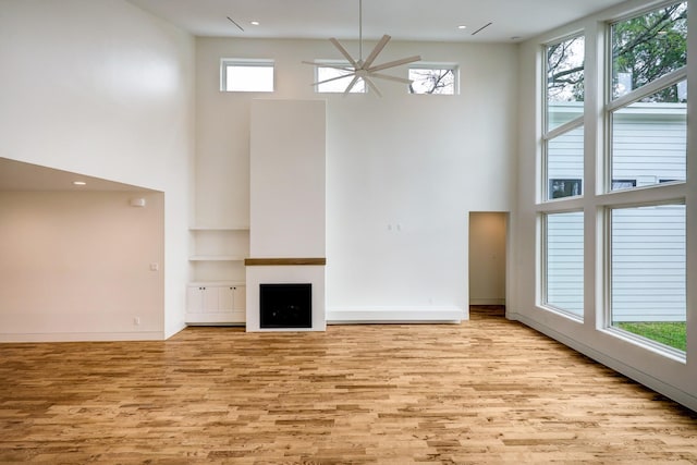 unfurnished living room with plenty of natural light, light wood finished floors, a fireplace, and a towering ceiling