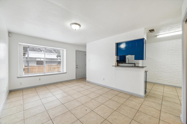 tiled empty room featuring baseboards, visible vents, a textured ceiling, and brick wall