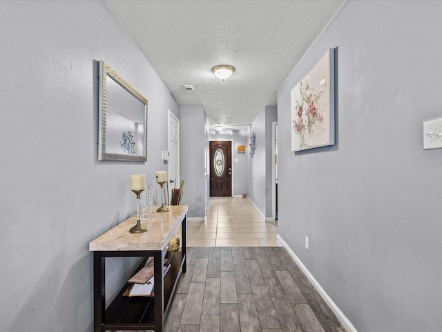 hall with light wood-type flooring, visible vents, a textured ceiling, and baseboards