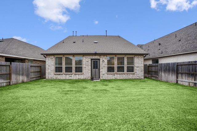 back of house with a fenced backyard, a shingled roof, a lawn, and brick siding