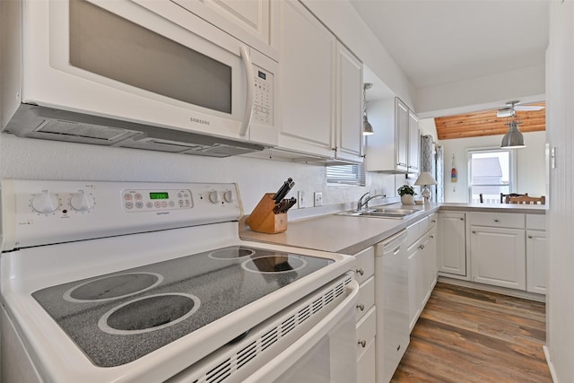 kitchen with white appliances, a sink, white cabinetry, light countertops, and dark wood-style floors