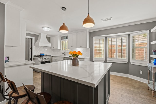 kitchen with hanging light fixtures, custom exhaust hood, light stone countertops, and white cabinets