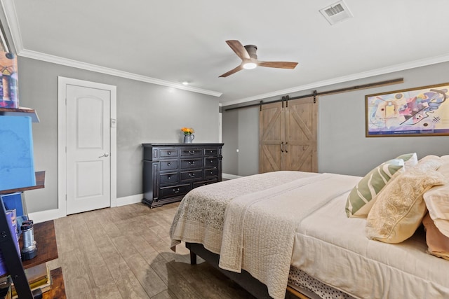 bedroom with a barn door, wood finished floors, visible vents, baseboards, and crown molding