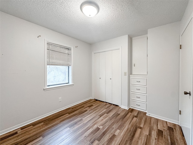 unfurnished bedroom with a closet, baseboards, a textured ceiling, and light wood finished floors