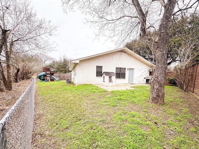 rear view of property with brick siding, a lawn, a playground, and a fenced backyard