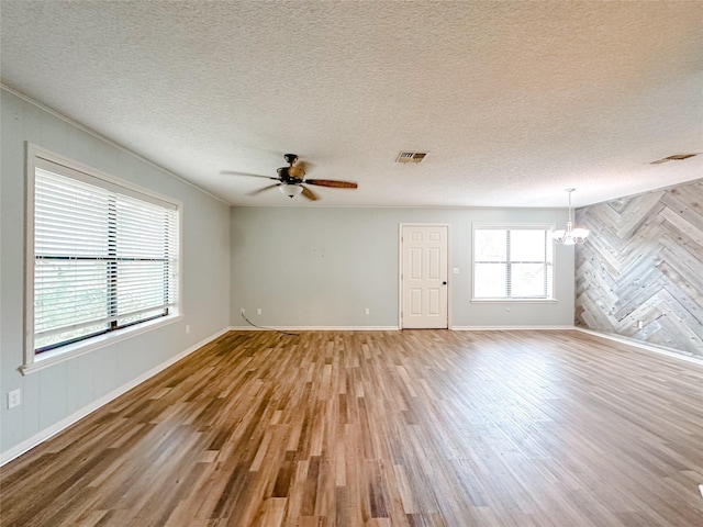 unfurnished room featuring ceiling fan with notable chandelier, visible vents, a textured ceiling, and wood finished floors