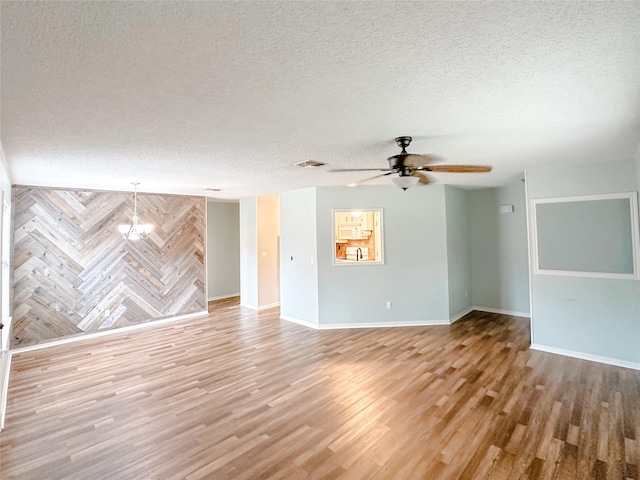 empty room with a textured ceiling, ceiling fan with notable chandelier, wood finished floors, visible vents, and baseboards