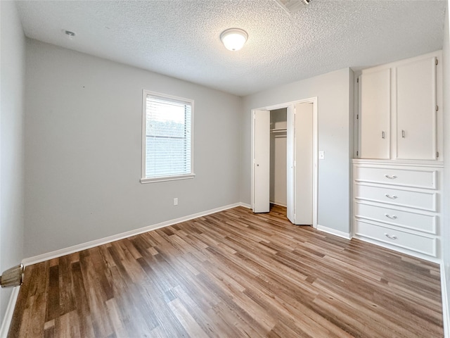 unfurnished bedroom featuring light wood finished floors, a textured ceiling, baseboards, and a closet