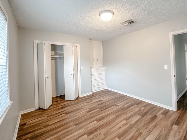 unfurnished bedroom featuring light wood-type flooring, a closet, a textured ceiling, and baseboards