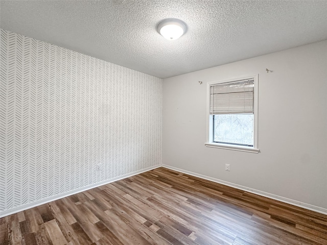 empty room with a textured ceiling, an accent wall, wood finished floors, and baseboards