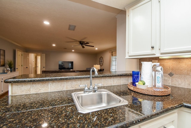 kitchen featuring visible vents, dark stone countertops, a peninsula, white cabinetry, and a sink