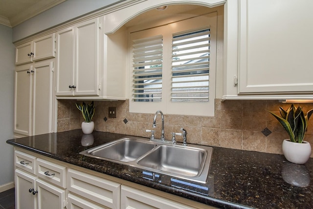 kitchen with dark stone countertops, a sink, decorative backsplash, and ornamental molding