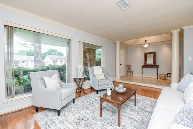 living area featuring crown molding, visible vents, decorative columns, and wood finished floors