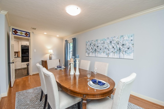 dining space with baseboards, a textured ceiling, wood finished floors, and crown molding