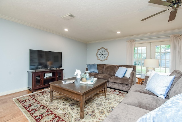 living room with ornamental molding, light wood finished floors, visible vents, and baseboards