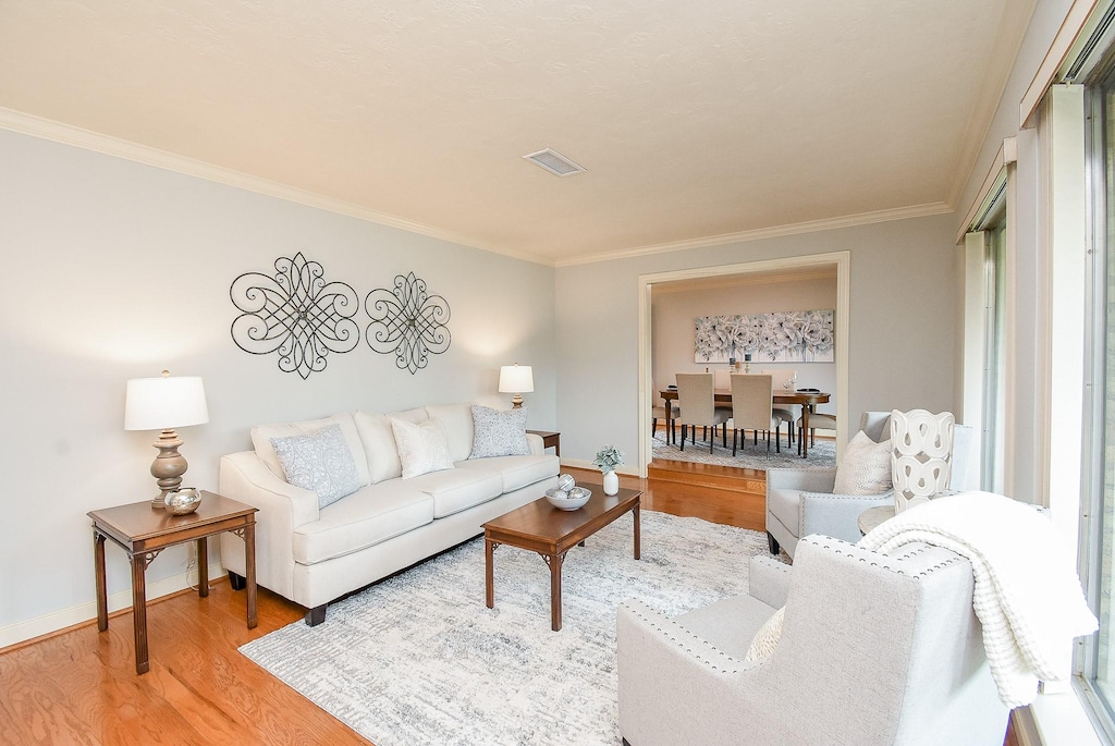 living area with baseboards, visible vents, ornamental molding, and wood finished floors