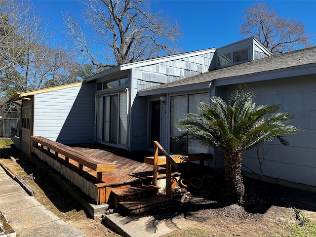 view of side of property with roof with shingles and a wooden deck