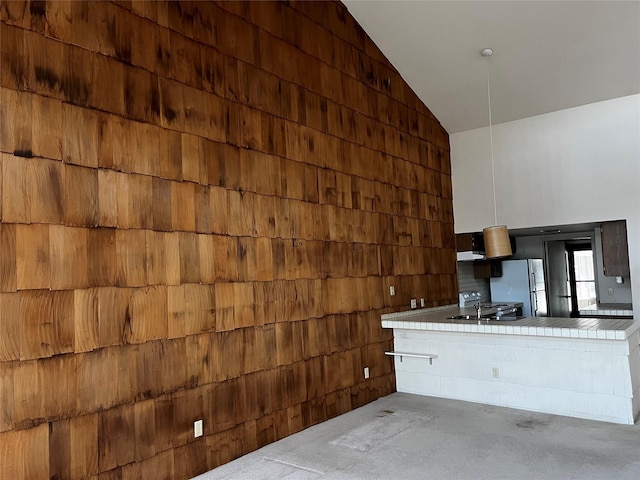 kitchen featuring tile counters, freestanding refrigerator, a sink, high vaulted ceiling, and concrete floors