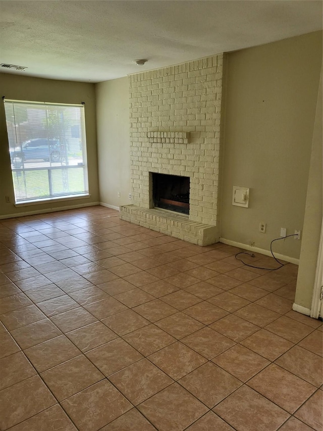 unfurnished living room featuring light tile patterned floors, a textured ceiling, visible vents, baseboards, and a brick fireplace