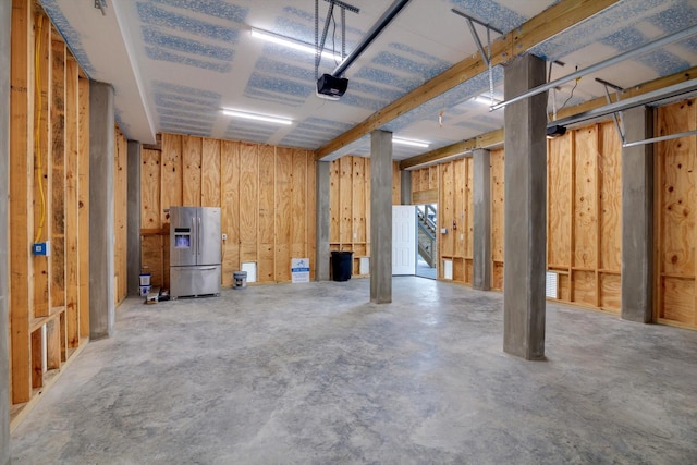 basement featuring a garage and stainless steel refrigerator with ice dispenser