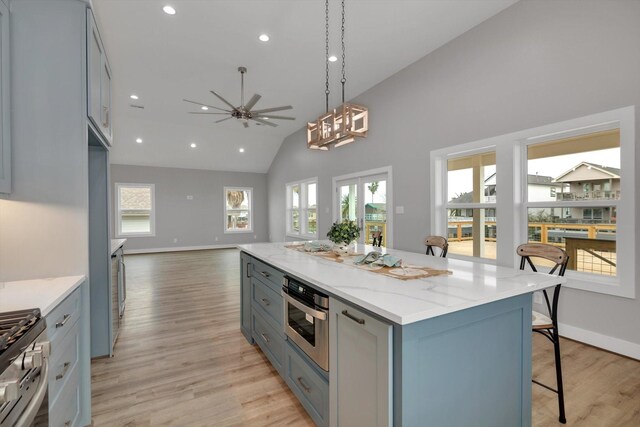 kitchen featuring light stone counters, stainless steel appliances, open floor plan, a center island, and decorative light fixtures