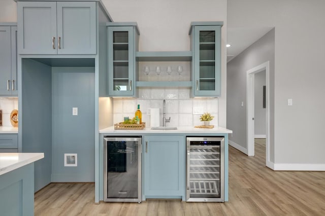 kitchen featuring light countertops, wine cooler, a sink, and glass insert cabinets