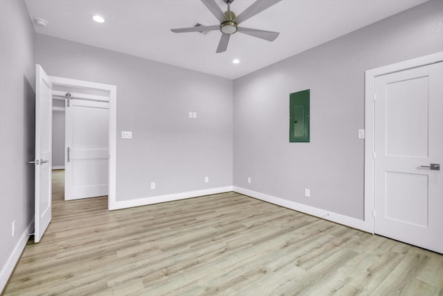 unfurnished bedroom with recessed lighting, light wood-style flooring, a barn door, electric panel, and baseboards