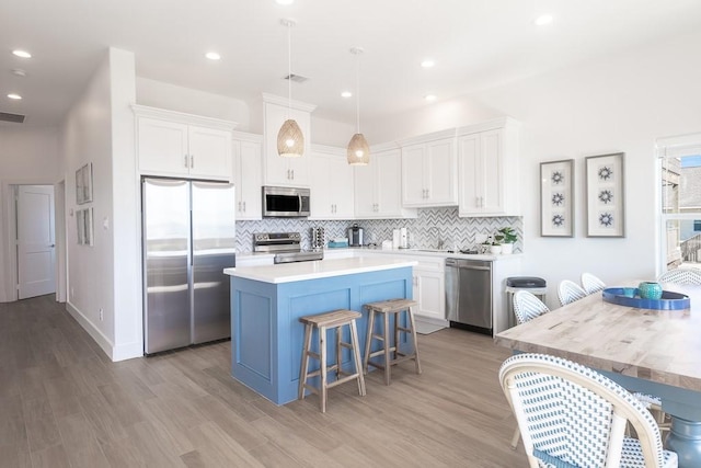 kitchen with white cabinets, a center island, decorative light fixtures, stainless steel appliances, and light countertops