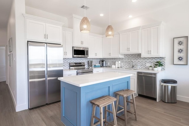 kitchen featuring stainless steel appliances, light countertops, white cabinetry, and decorative light fixtures