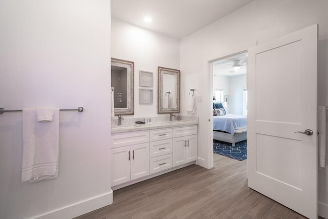 ensuite bathroom featuring double vanity, ensuite bath, a sink, and wood finished floors