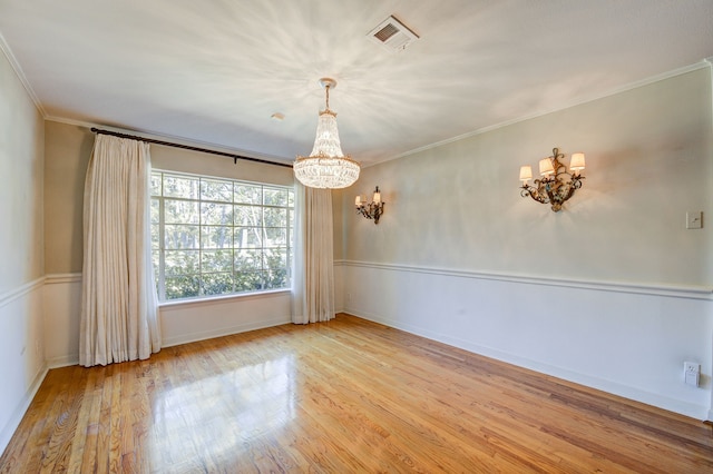 spare room featuring light wood-style flooring, visible vents, baseboards, ornamental molding, and an inviting chandelier