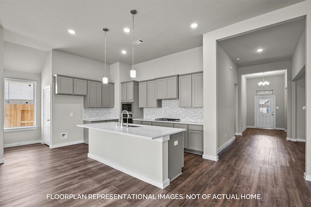 kitchen with an island with sink, dark wood-type flooring, decorative light fixtures, light countertops, and stainless steel gas stovetop