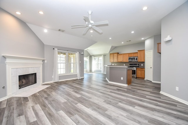 unfurnished living room with lofted ceiling, ceiling fan, a fireplace, visible vents, and light wood-type flooring