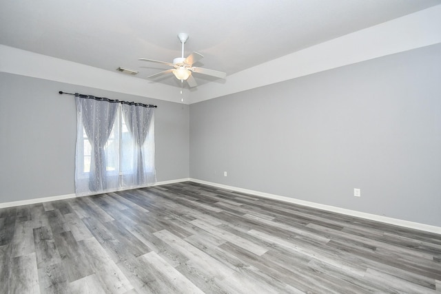 empty room featuring a ceiling fan, wood finished floors, visible vents, and baseboards