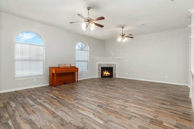 unfurnished living room with a ceiling fan, a lit fireplace, baseboards, and wood finished floors