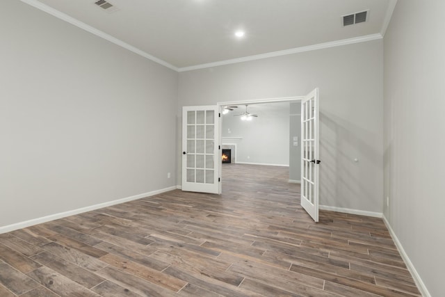 unfurnished room with visible vents, wood finished floors, a lit fireplace, crown molding, and french doors