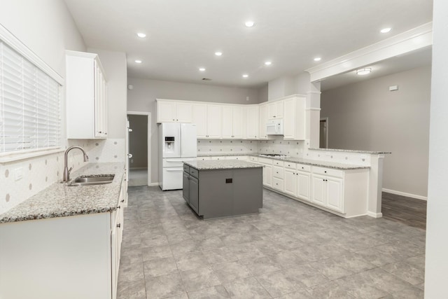 kitchen with white appliances, a sink, light stone counters, and a center island