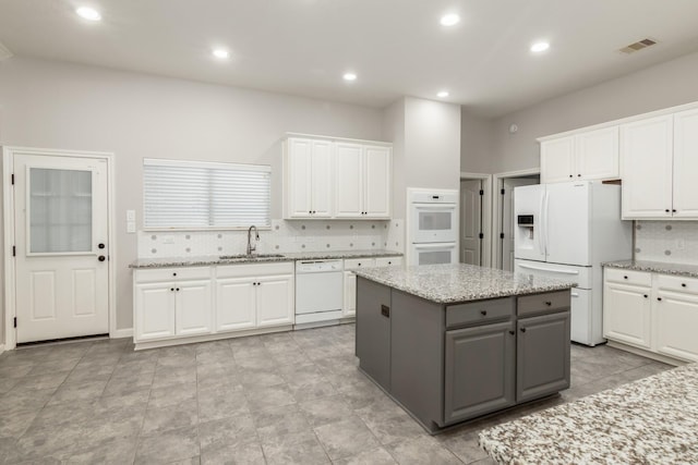 kitchen featuring visible vents, gray cabinetry, white cabinetry, a sink, and white appliances