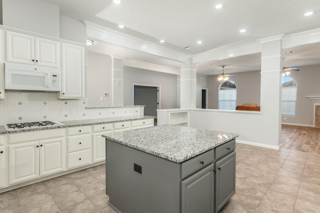 kitchen with white microwave, a kitchen island, ornamental molding, gray cabinets, and decorative backsplash