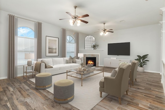 living room featuring ceiling fan, a lit fireplace, baseboards, and wood finished floors