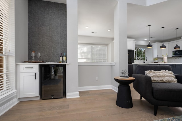 bar featuring stainless steel microwave, hanging light fixtures, a bar, light wood-type flooring, and beverage cooler