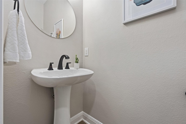 bathroom featuring a textured wall, a sink, and baseboards