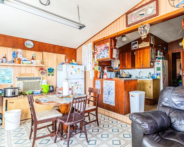 kitchen with freestanding refrigerator, vaulted ceiling, wood walls, and light floors